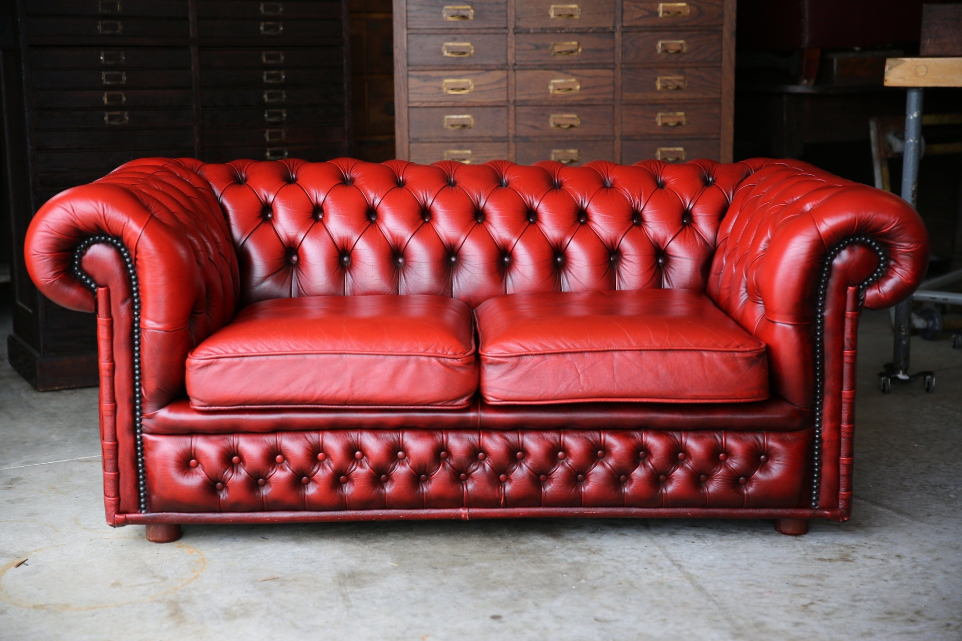 Vintage Chesterfield Sofa red leather couch loveseat wood legs nailhead trim office living room space tufted sports bar loft cushions settee