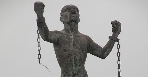 Statue Monument: Weathered Bronze with Broken Chains and Raised Arms.