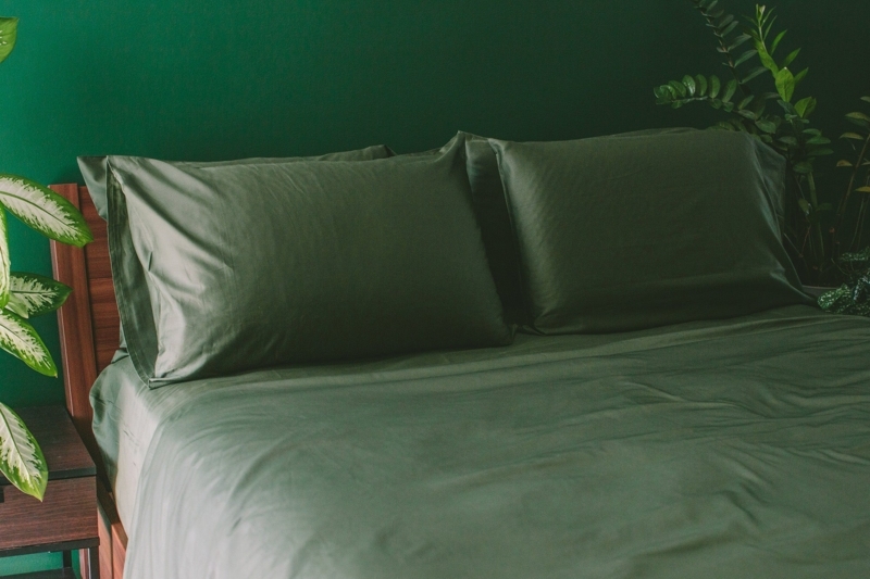 Moss Green Sateen Sheet Set Stack against Textured Plaster Wall