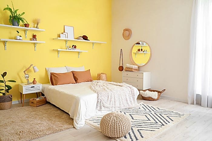 Bohemian Bedroom with Yellow Accent Wall, Layered Rugs, and Knit Pouf