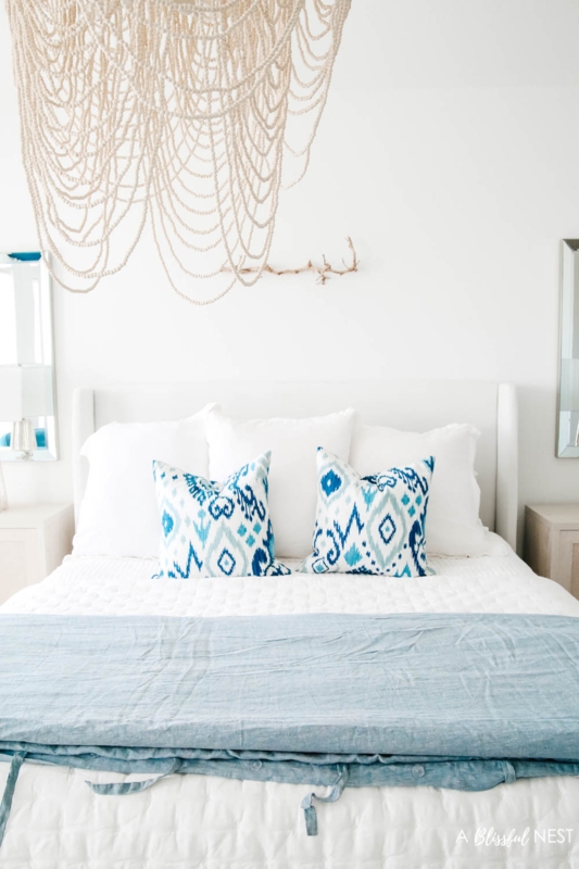 Cascading Beaded Chandelier above White Wingback Bed with Ikat Pillows