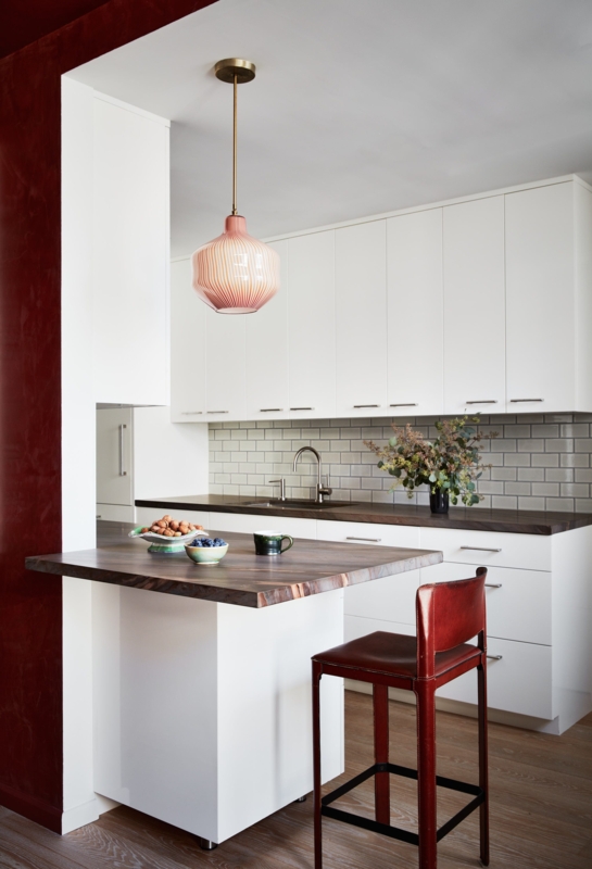 Eclectic White Kitchen with Red Accent Wall and Ribbed Glass Pendant