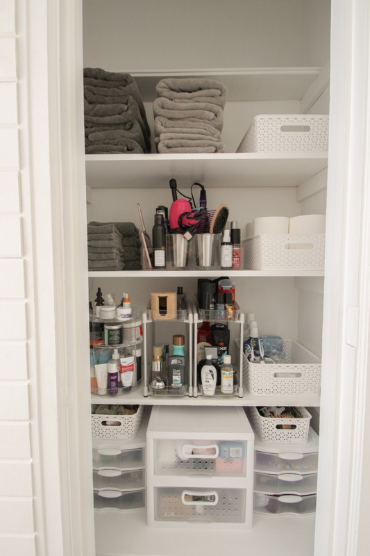 Linen Closet organized with white perforated baskets and tiered shelves. SEO: neat linen closet.