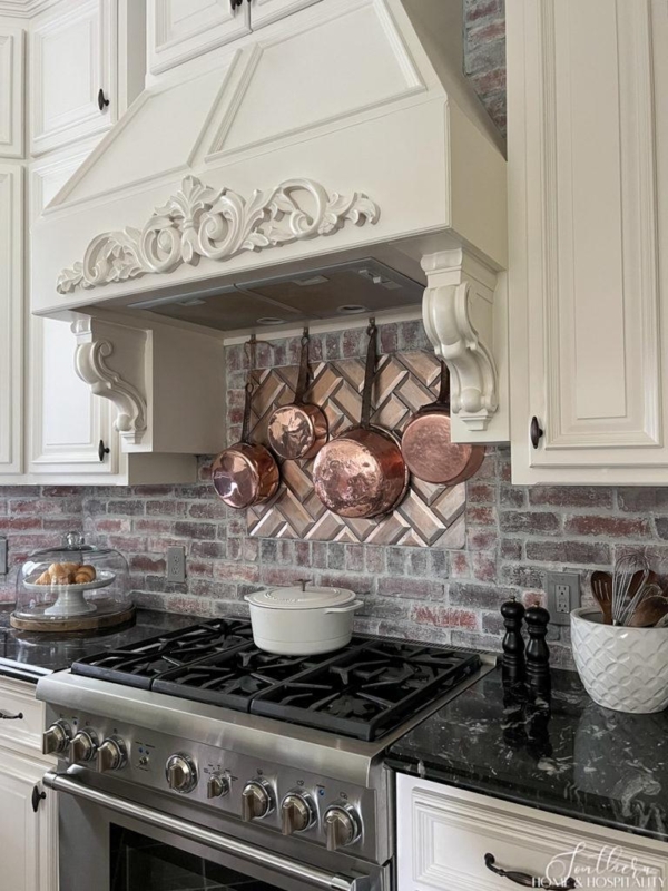 Ornate Range Hood with Copper Pot Display on Brick Backsplash