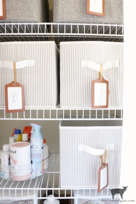 Storage Bins with luggage tag labels on striped fabric. SEO: linen closet organization ideas.