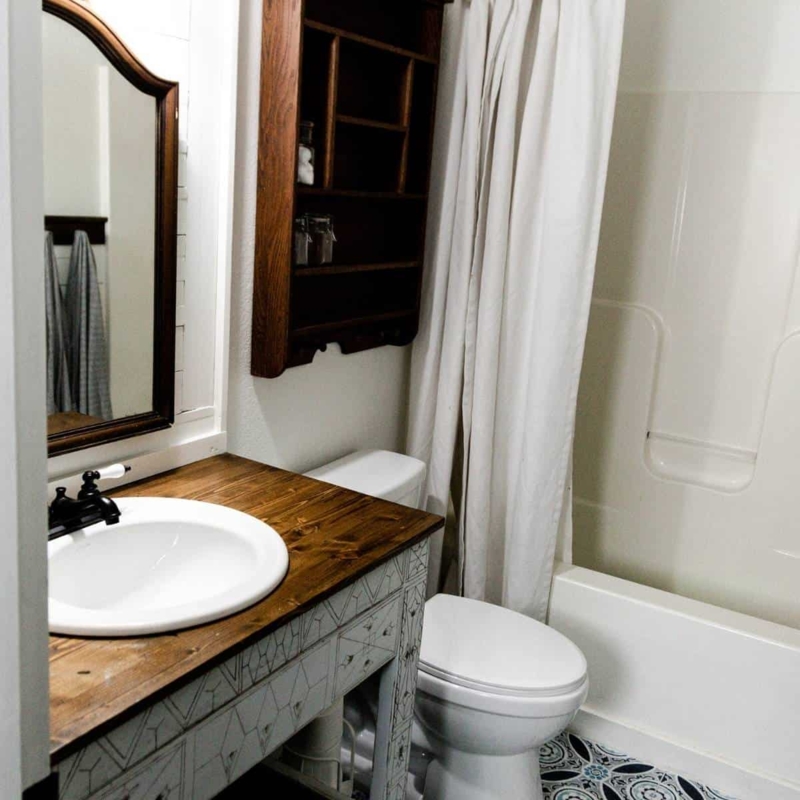 Farmhouse Bathroom with Patterned Floor Tile and Dark Arched Mirror