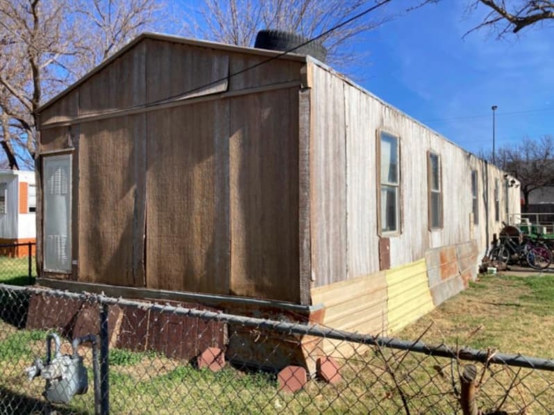 Mobile Home: Weathered Vertical Siding & Mismatched Skirting.
