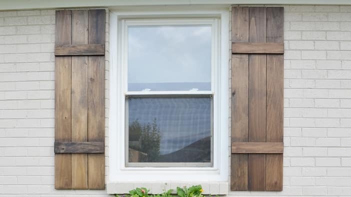 Rustic Stained Wood Exterior Shutters with Grain Texture on Brick Wall