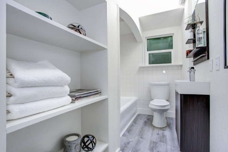 Small Bathroom with Built-In White Shelving and Arched Tub Alcove