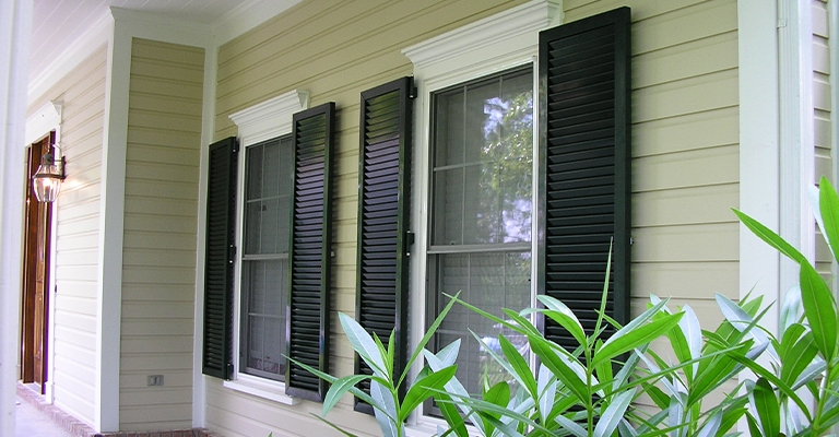 Traditional Black Louvered Exterior Window Shutters against Tan Siding