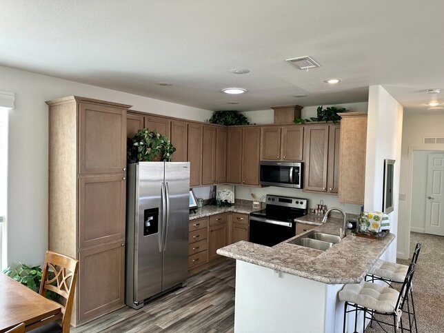 U-Shaped Mobile Home Kitchen: Breakfast Bar Counter, Wood Toned Cabinets.