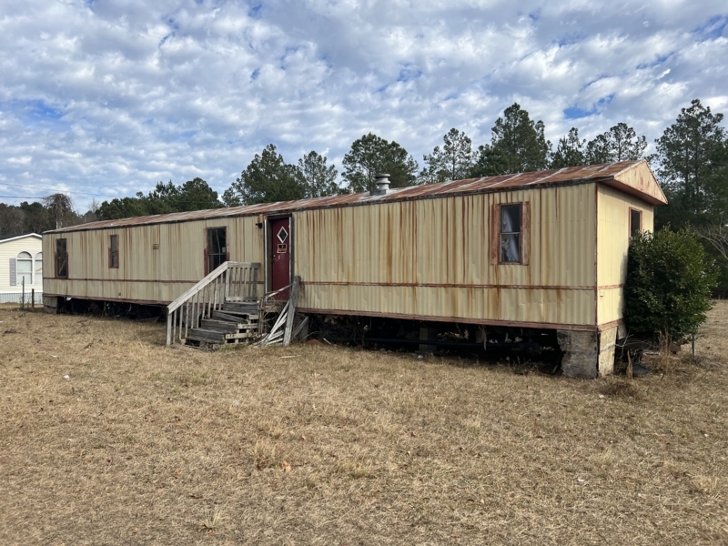 Weathered Mobile Home Exterior with Red Entry Door and Rustic Wooden Steps