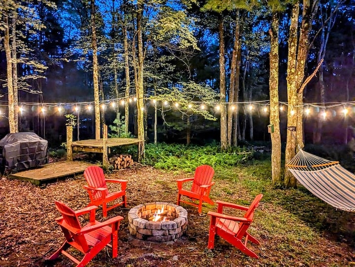 Wooded Fire Pit Area with Red Adirondack Chairs and String Lights
